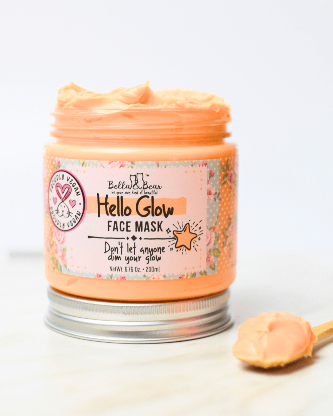 Open jar of Bella and Bear Hello Glow face mask in peach cream with wooden spatula showing texture