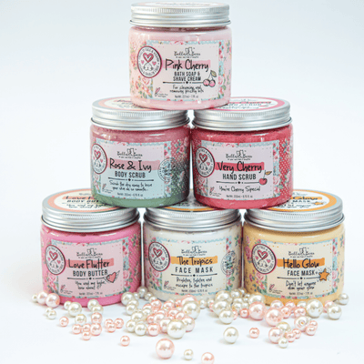 Stack of Bella and Bear skincare jars including Hello Glow face mask among colorful body scrubs and butters